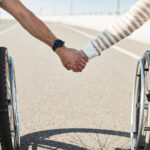 Paar im Rollstuhl hält sich liebevoll an den Händen – Nahaufnahme im Freien