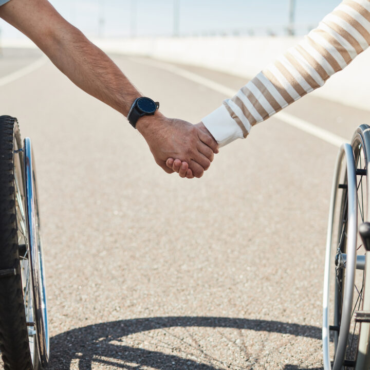Paar im Rollstuhl hält sich liebevoll an den Händen – Nahaufnahme im Freien