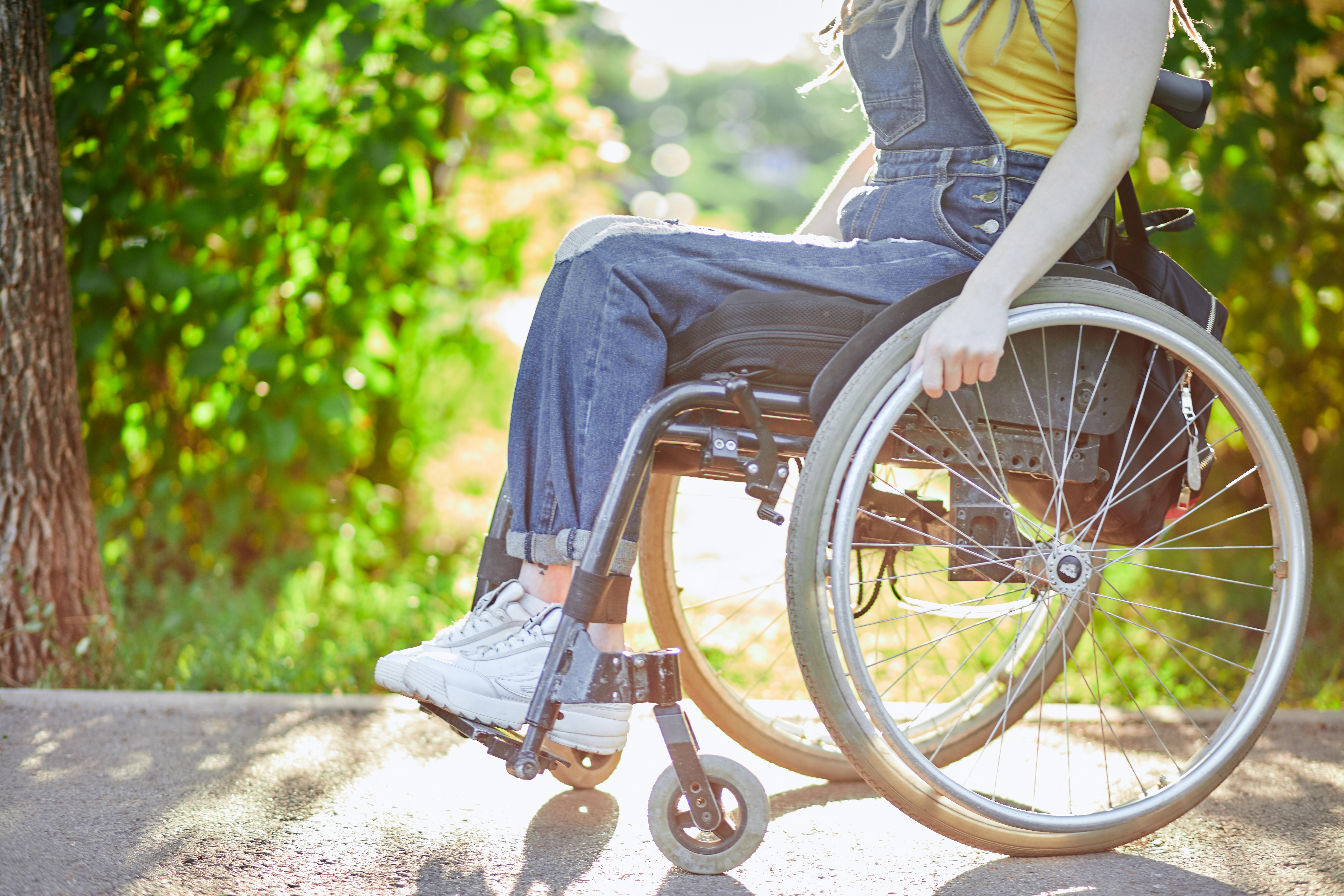 Frau sitzt im Rollstuhl auf der Straße – Seitenansicht mit Nahaufnahme der Räder