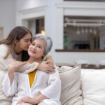 Mutter und Tochter umarmen sich lächelnd auf dem Sofa im Wohnzimmer