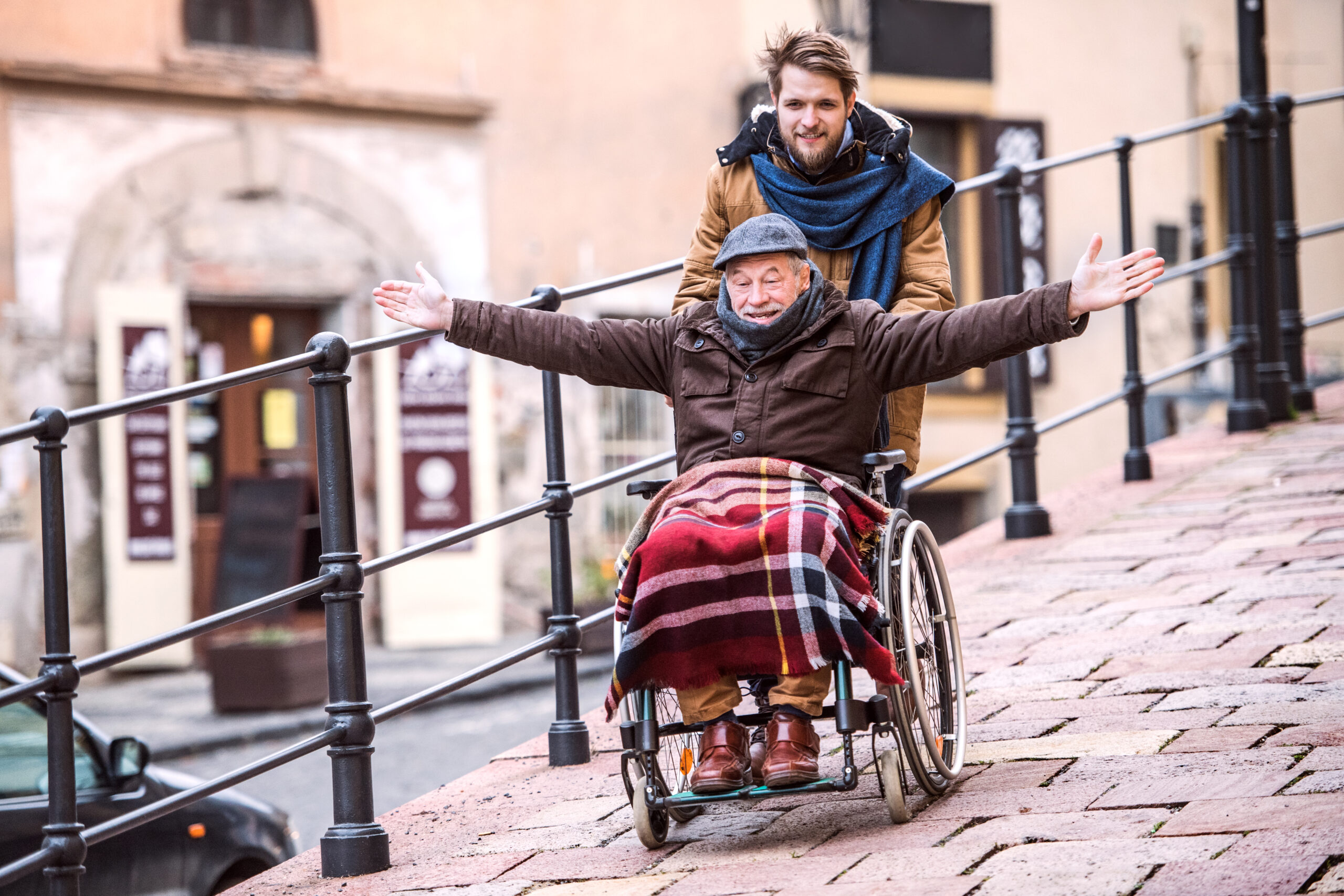 Älterer Vater im Rollstuhl beim Spaziergang mit Sohn und Pflegeperson