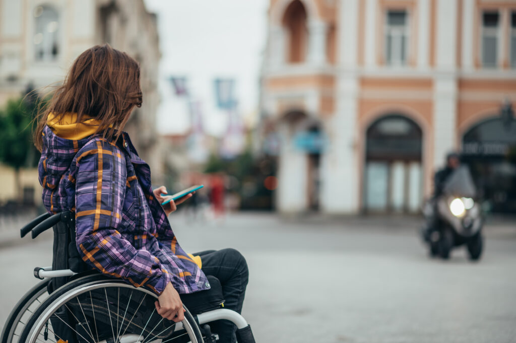 Junge Frau im Rollstuhl telefoniert mit dem Smartphone in der Stadt